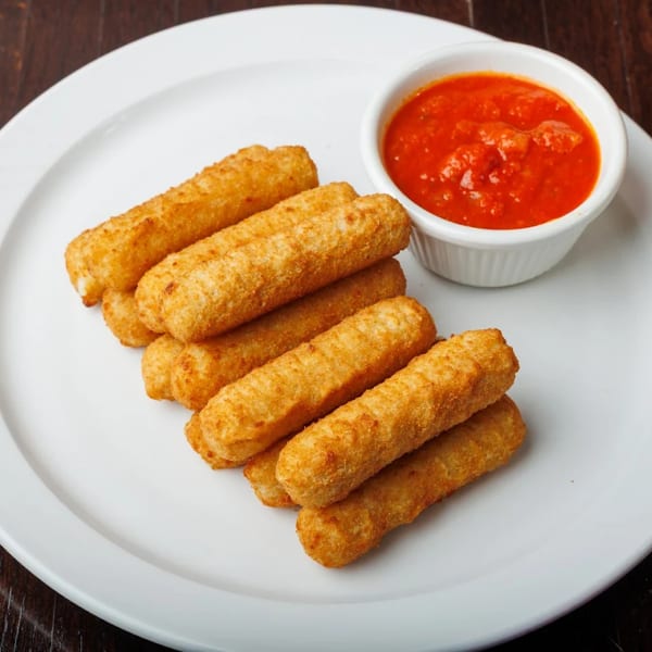 Golden-brown mozzarella sticks piled on a white plate with a side of red marinara sauce.