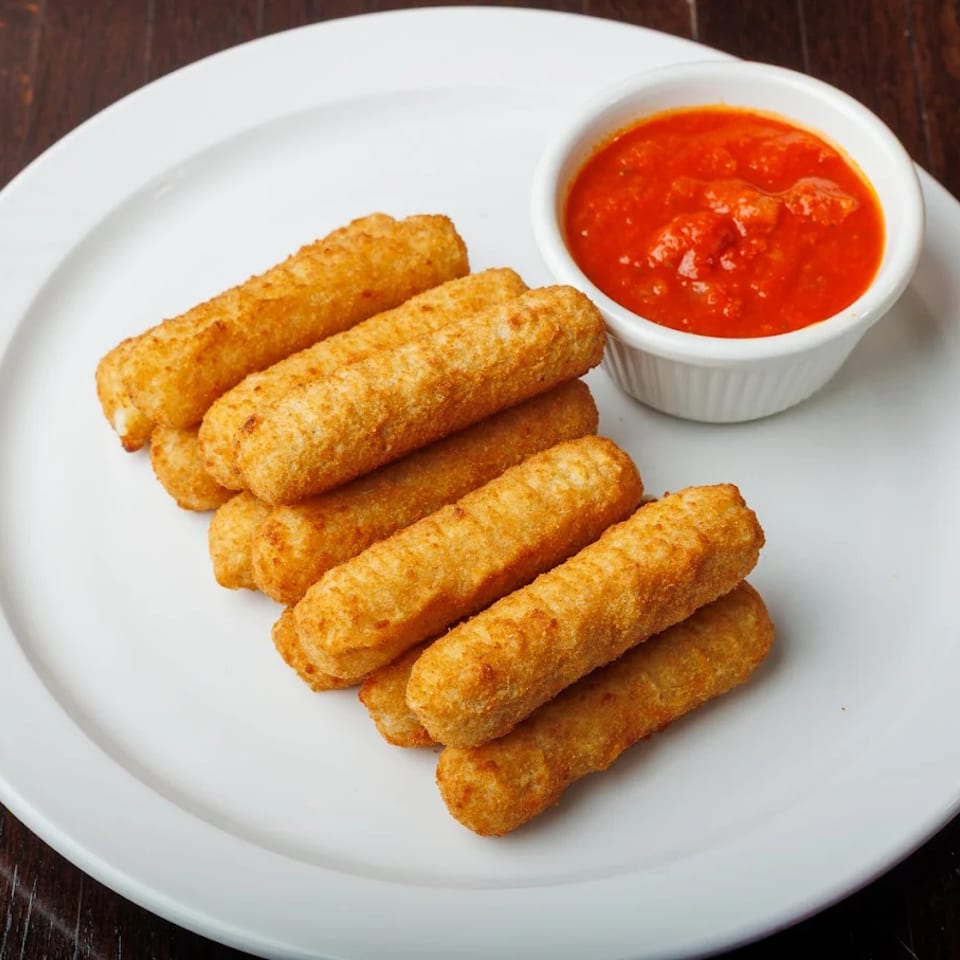 Golden-brown mozzarella sticks piled on a white plate with a side of red marinara sauce.