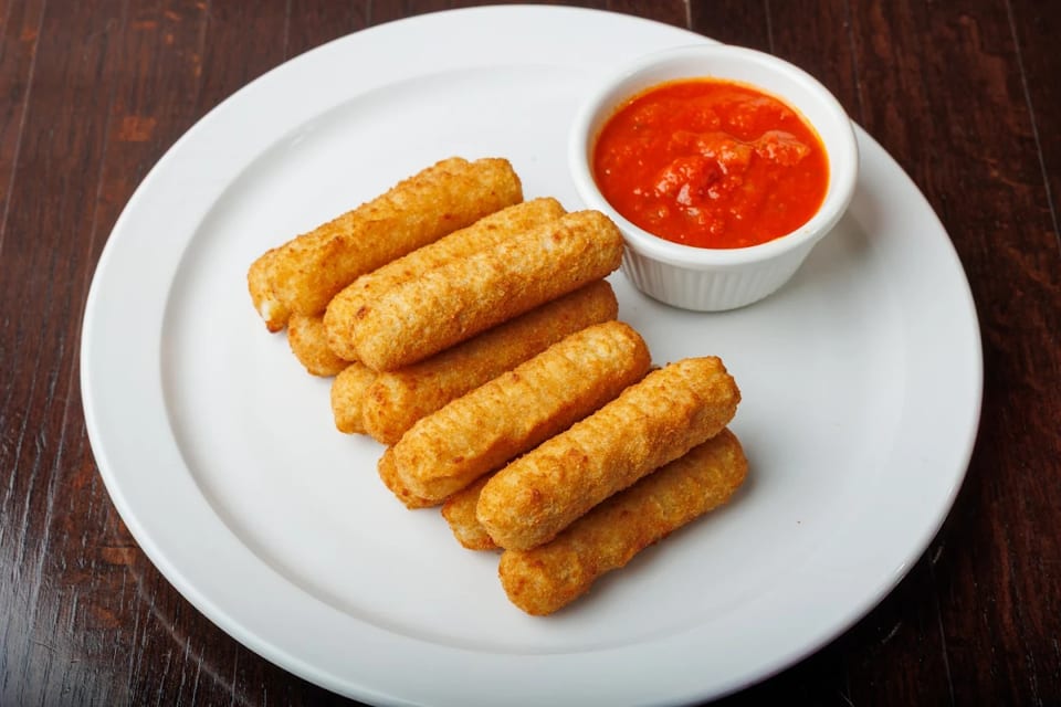 Golden-brown mozzarella sticks piled on a white plate with a side of red marinara sauce.