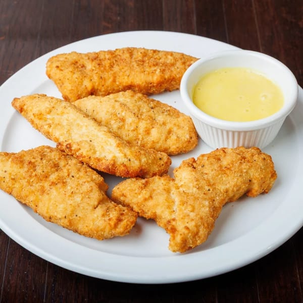 Crispy chicken tenders with a side of honey mustard dipping sauce on a white plate.
