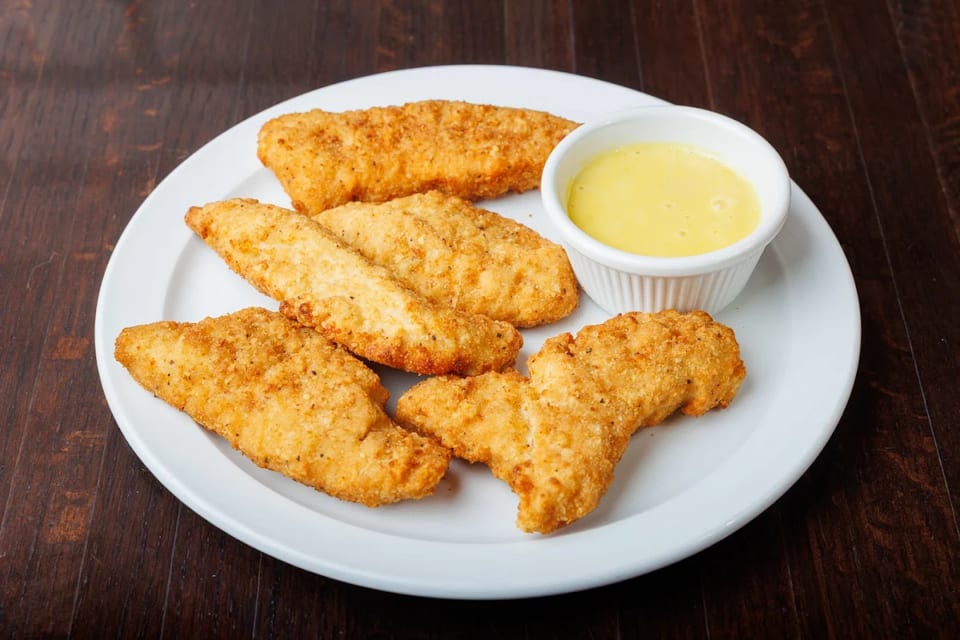 Crispy chicken tenders with a side of honey mustard dipping sauce on a white plate.
