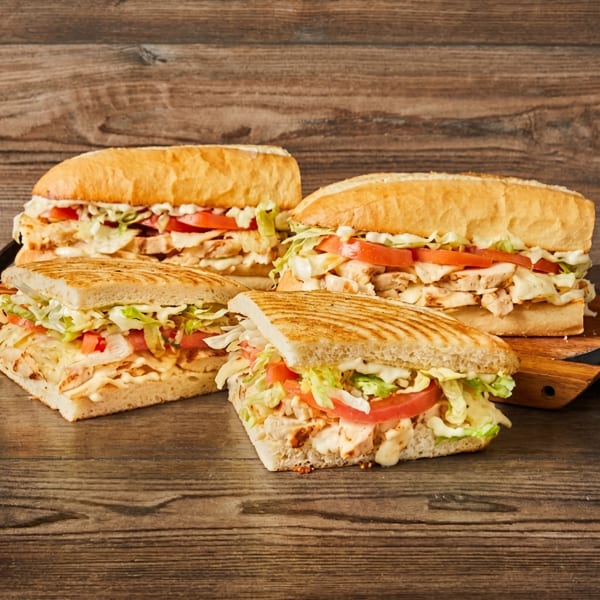 Four chicken sandwiches with lettuce, tomato, and sauce on a rustic wooden table.