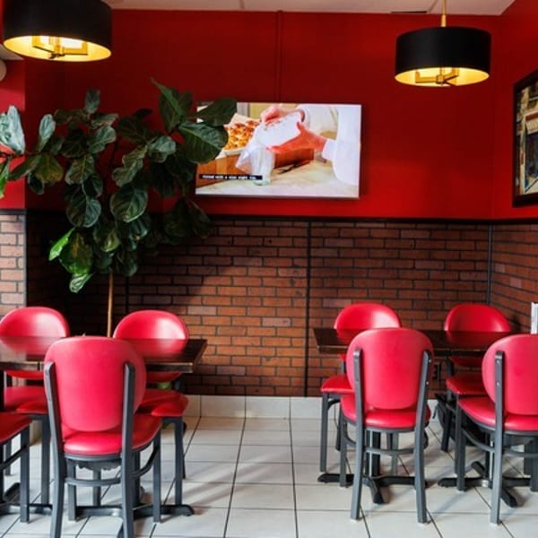 Restaurant interior with red walls, brick wainscoting, red chairs, dark tables, and a TV showing food.