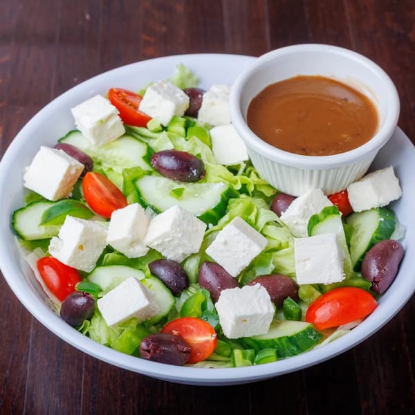 A vibrant Greek salad with feta, olives, tomatoes, cucumbers, and lettuce, served with dressing.