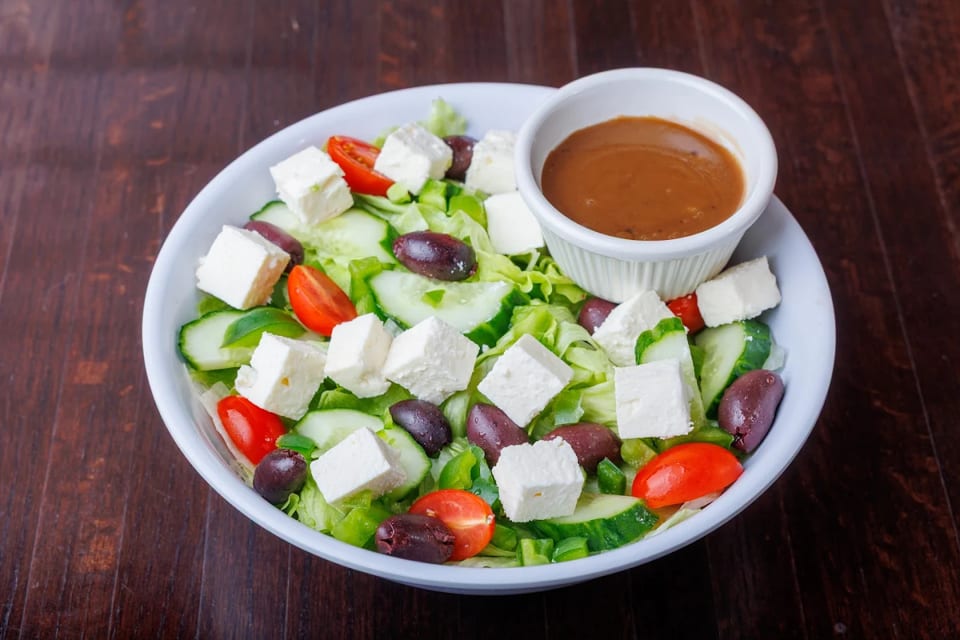 A vibrant Greek salad with feta, olives, tomatoes, cucumbers, and lettuce, served with dressing.