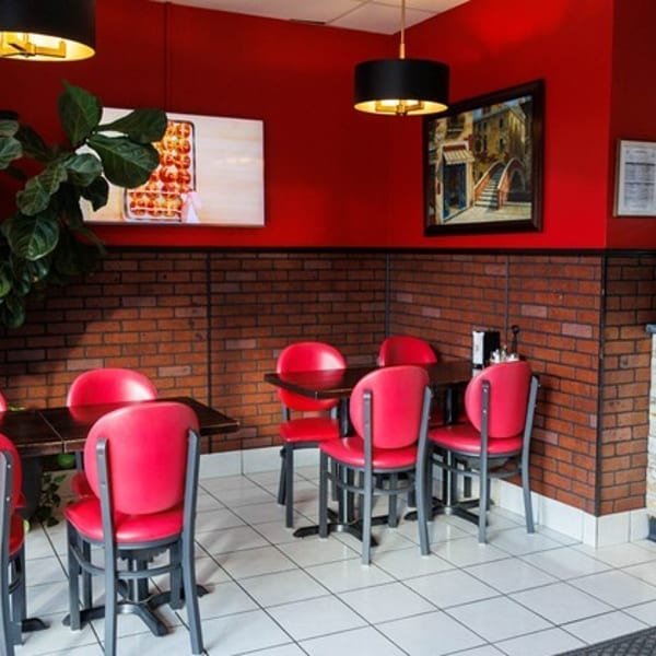 Restaurant interior with red walls, brick wainscoting, red chairs, dark tables, and a display case.